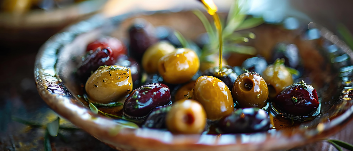 ELMAR premium Greek olives in a selection of green and black varieties, drizzled with golden olive oil and fresh herbs, showcasing authentic Mediterranean flavour and quality.
